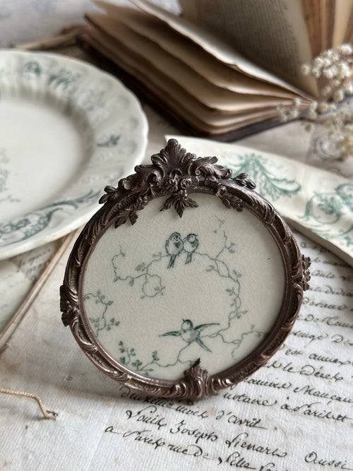 Antique round bronze frame with Gien ironstone motif, scrollwork pattern